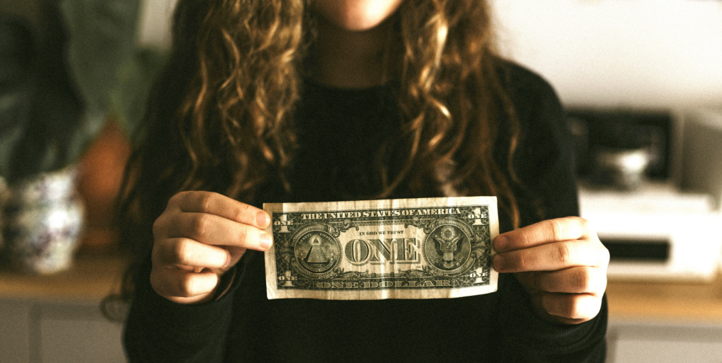 Young girl holding a one dollar bill between her fingers and showing the value of a dollar.