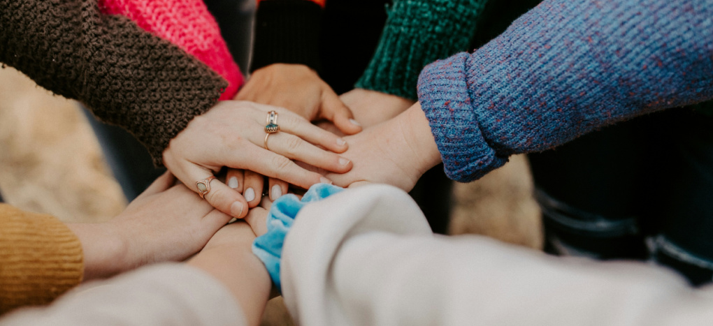 Image of hands coming together to support one another in a circle.