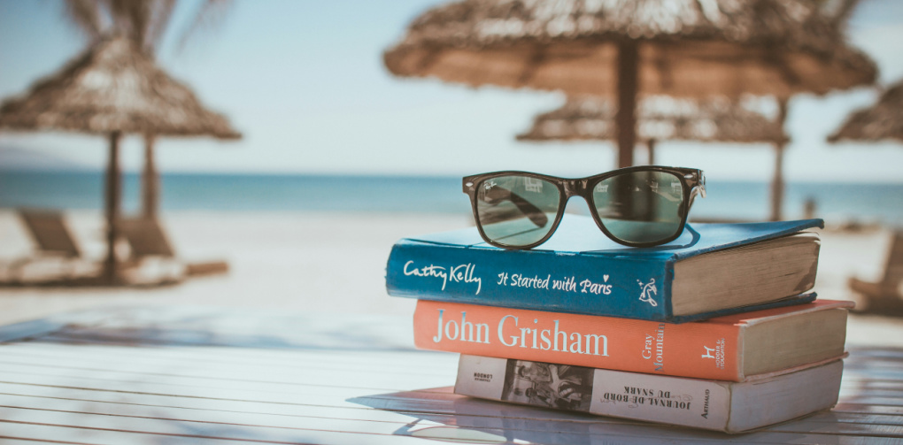 Image of a stack of books on a beach table with the ocean in the background