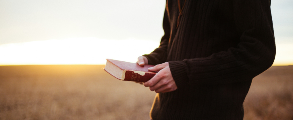 Image of a man in a field with the sunrise and a Bible